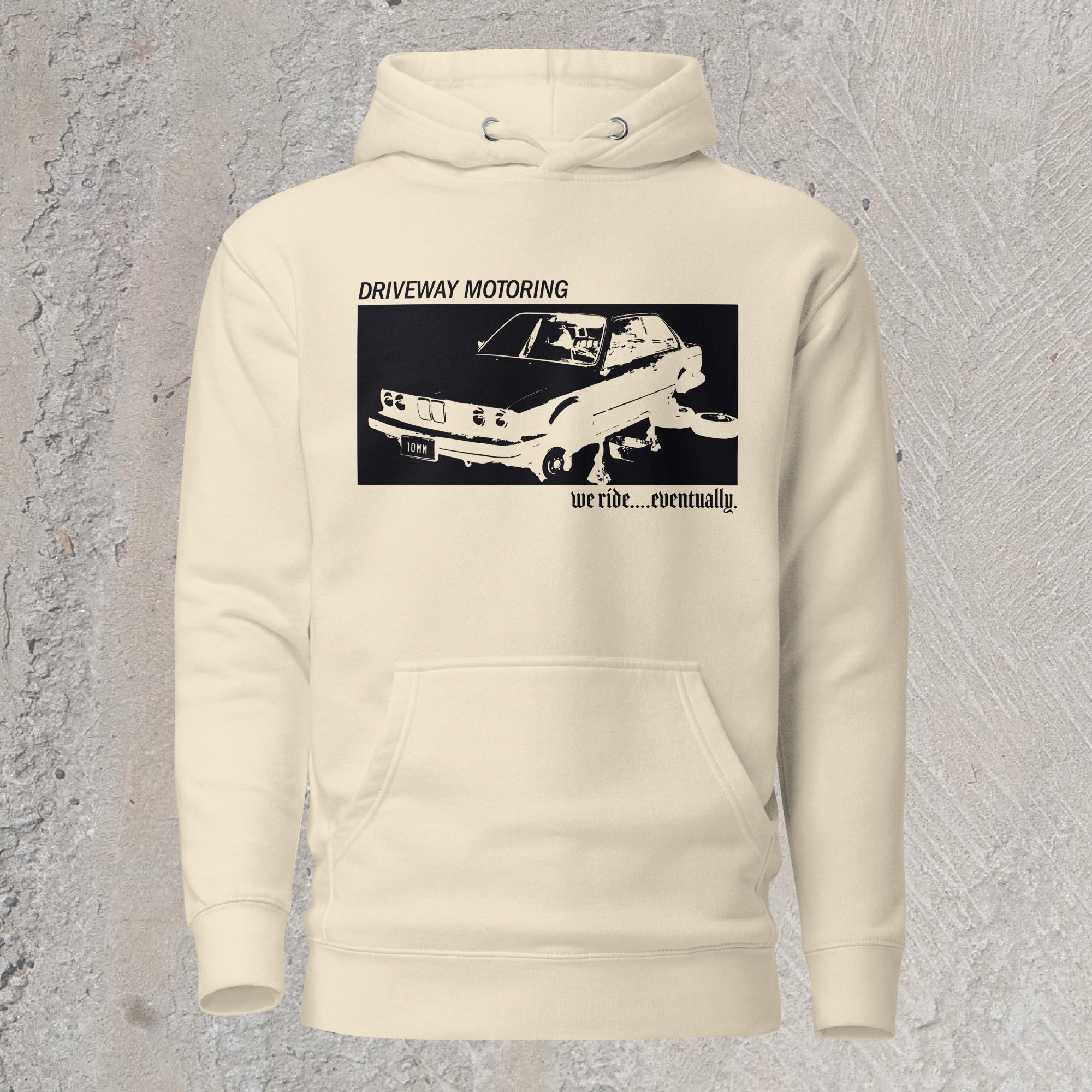 10mm funny graphic cream-colored hoodie sweatshirt with BMW car on jack stands with text "Driveway motoring. We ride...eventually"