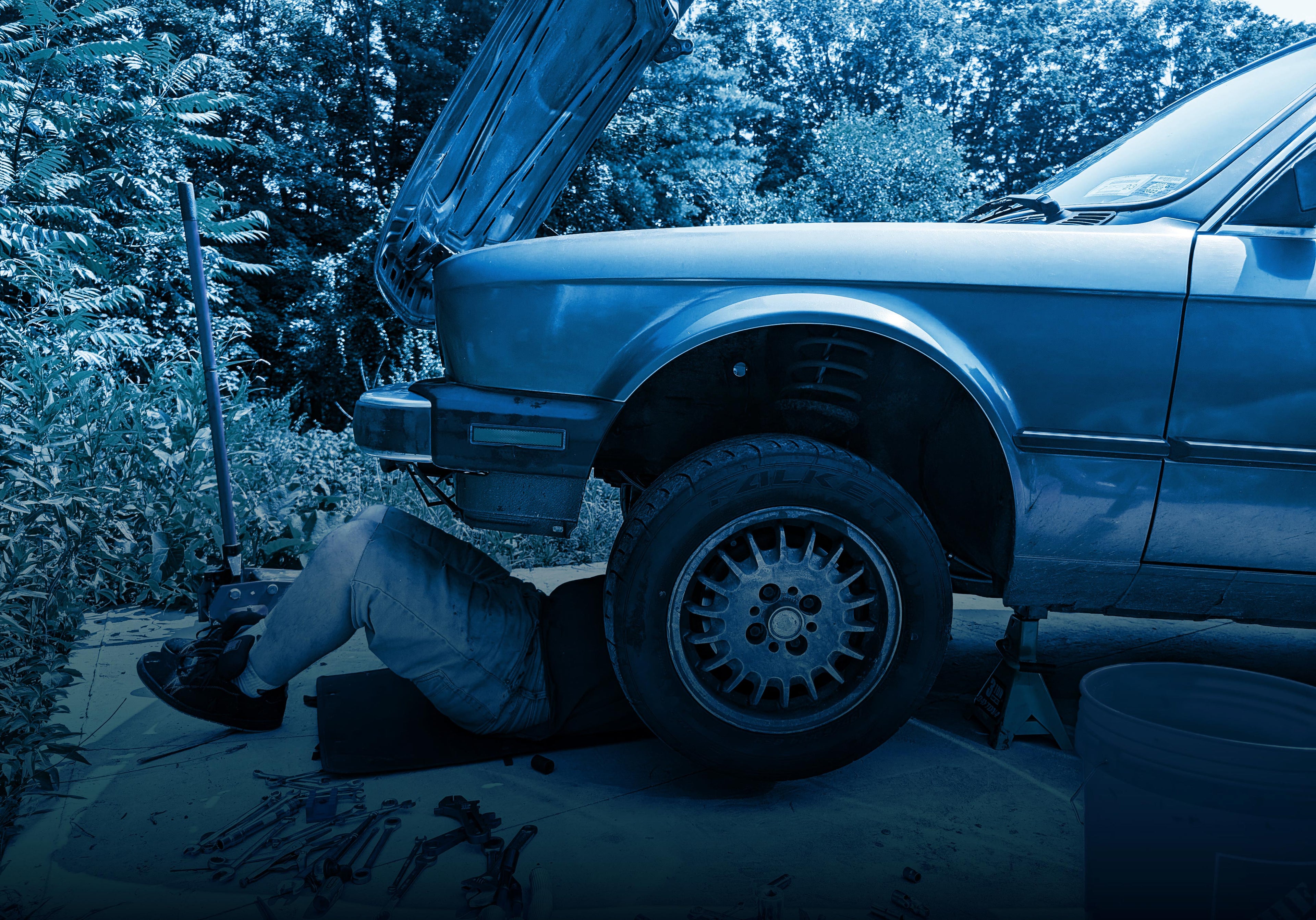 Person working on a car with the hood open in an outdoor setting