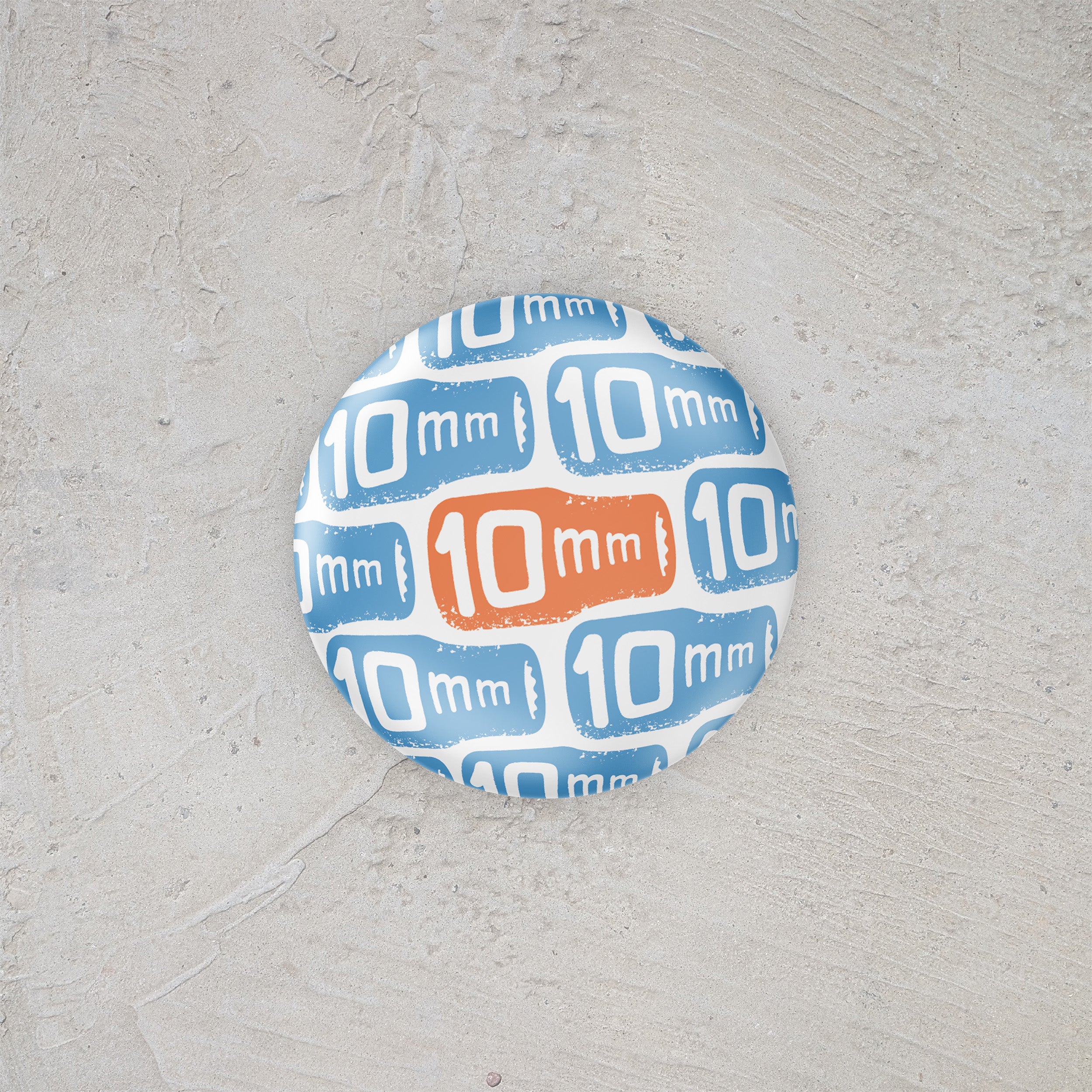 Pin button with '10 mm' pattern on a gray surface
